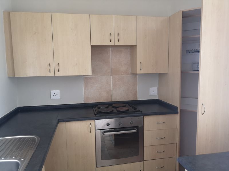 A functional kitchen featuring light wood-finish cabinetry, dark laminate countertops, a built-in oven with electric hob, and a dedicated pantry cupboard.