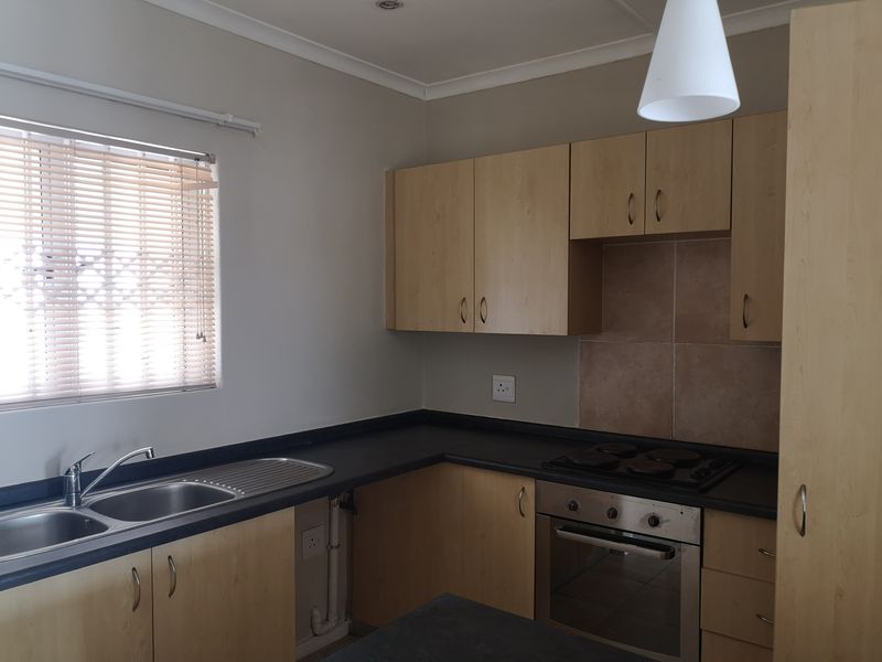 A functional kitchen featuring light wood-finish cabinetry, dark countertops, a built-in oven with electric hob, and a double stainless steel sink.