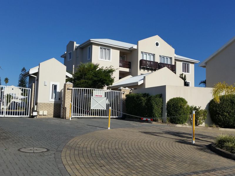 Front entrance view of the apartment complex featuring a secure gated access point, paved driveway, and multi-story building facade with balconies.