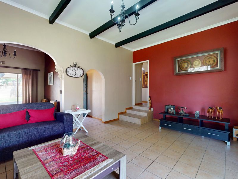 Spacious living room featuring ceramic tile flooring, exposed ceiling beams, and an arched entryway leading to adjacent living areas.