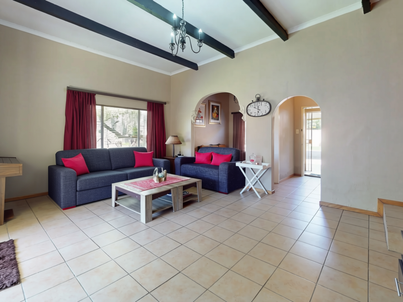Spacious living room featuring tiled flooring, exposed ceiling beams, and distinctive arched doorways leading to adjacent areas.