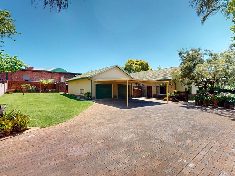 Front view of the property featuring a paved driveway, double garage, attached carport, and a well-maintained garden area.