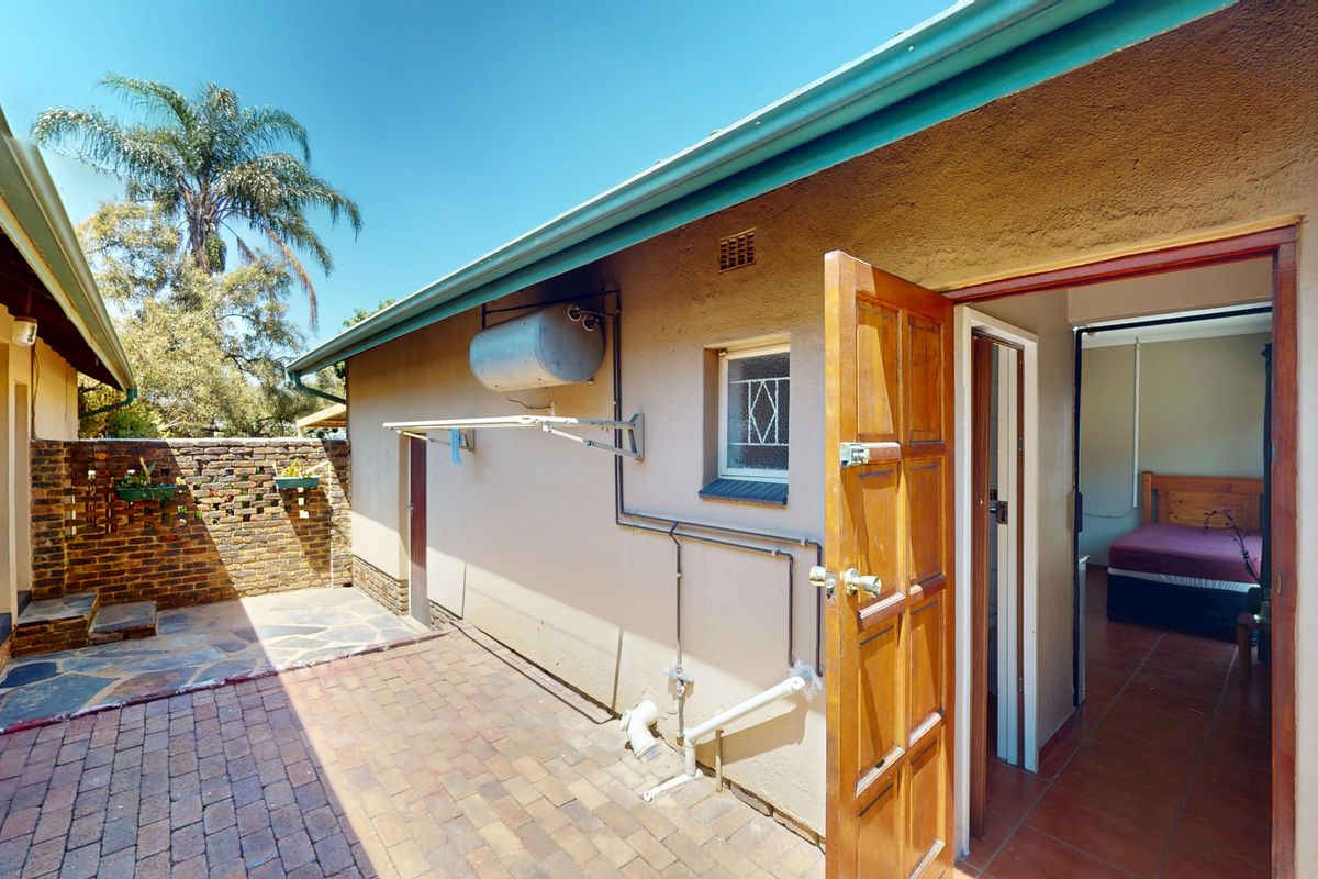 Rear exterior area featuring brick paving, a boundary wall, and access to the interior, equipped with an external geyser and wall-mounted washing line.