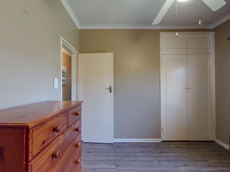 A bedroom featuring laminate flooring, built-in cupboards, and a ceiling fan, offering a neutral base for personalization.