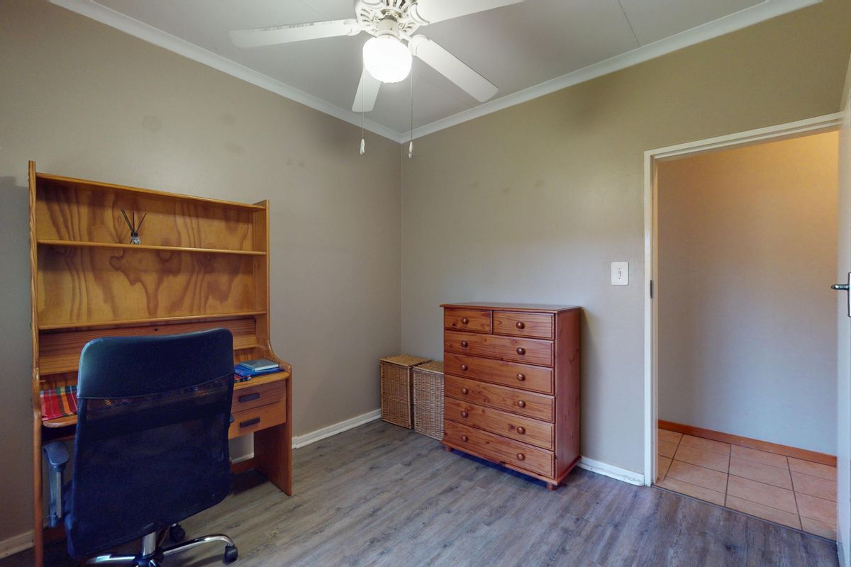 A functional bedroom featuring laminate flooring, a ceiling fan, and neutral wall tones, suitable for use as a home office or guest room.