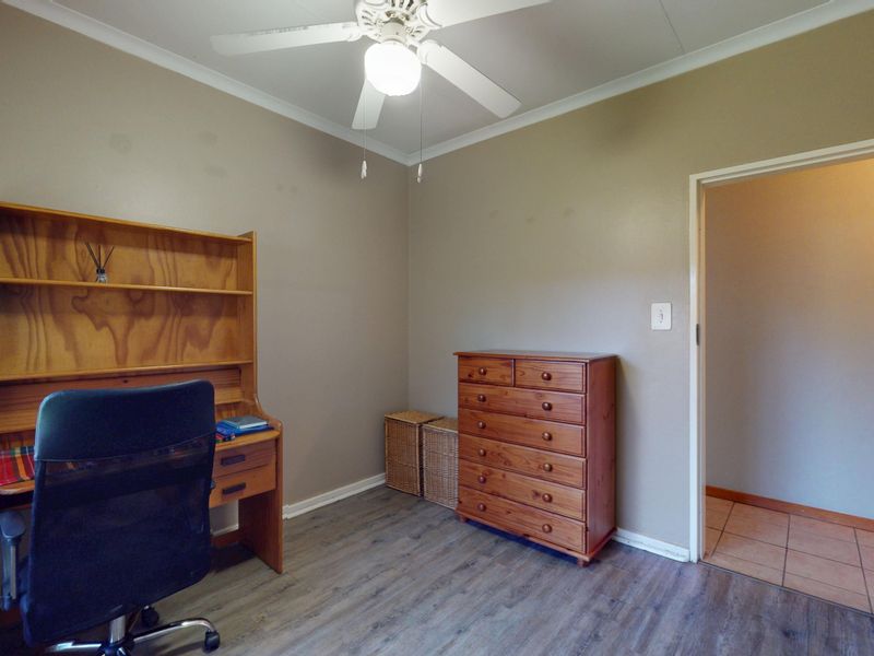 A functional bedroom featuring laminate flooring, a ceiling fan, and neutral wall tones, suitable for use as a home office or guest room.