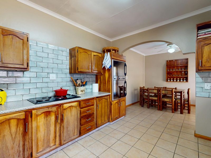 Open-plan kitchen and dining area featuring wooden cabinetry, built-in oven, electric hob, subway tile backsplash, and tiled flooring with a connecting archway.