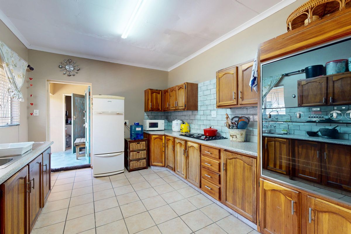 A functional kitchen featuring wooden cabinetry, built-in oven, hob, and tiled splashback, offering a practical layout with direct access to an outdoor area.