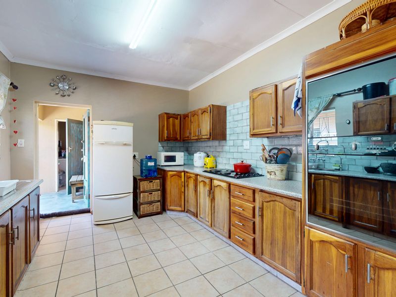 A functional kitchen featuring wooden cabinetry, built-in oven, hob, and tiled splashback, offering a practical layout with direct access to an outdoor area.