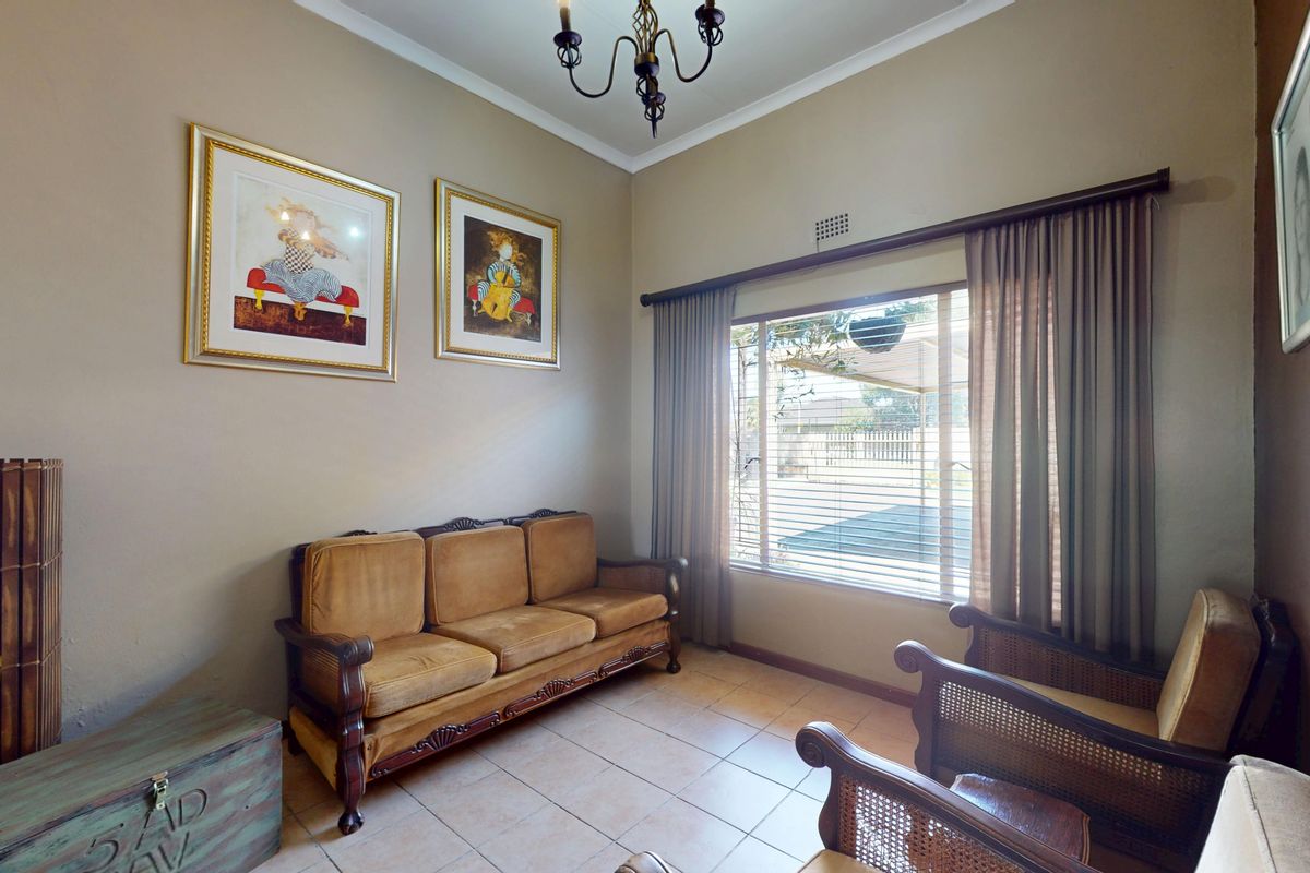 A living room featuring tiled flooring, neutral wall tones, and a large window with curtain rails, providing natural light to the space.
