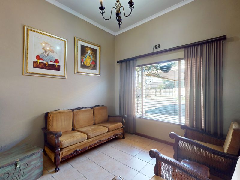 A living room featuring tiled flooring, neutral wall tones, and a large window with curtain rails, providing natural light to the space.