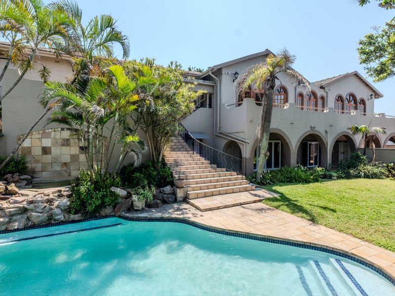 Spacious rear garden featuring a swimming pool, stone water feature, and a grand tiled staircase leading to an arched patio and upper balcony.