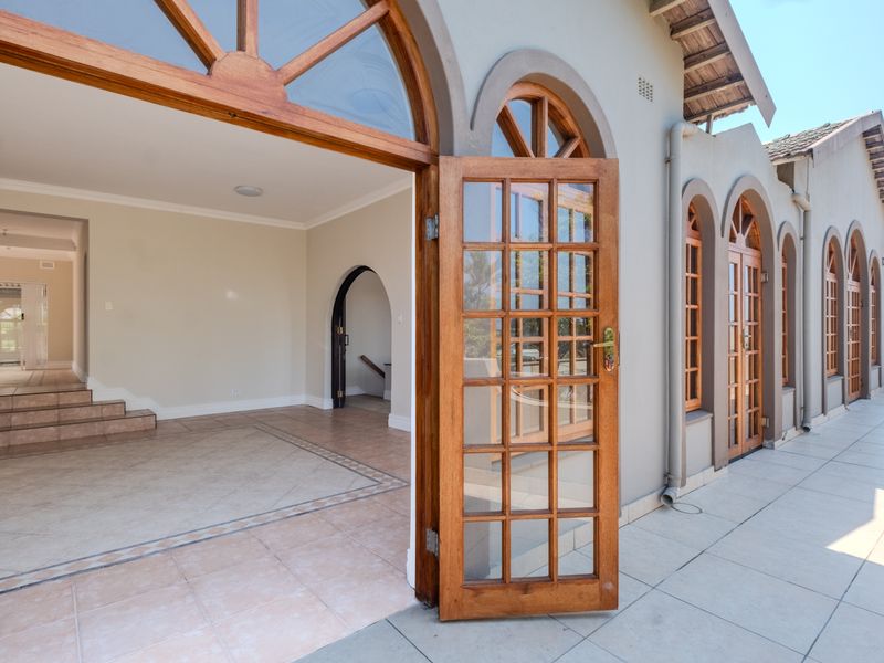 Spacious tiled patio featuring arched timber-framed glass doors leading into an open-plan interior living area with a staircase.