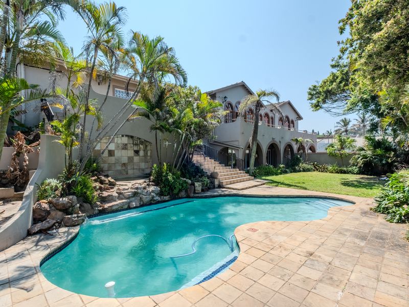 Spacious rear garden featuring a swimming pool, stone water feature, paved patio area, and an external staircase leading to the upper level balcony.