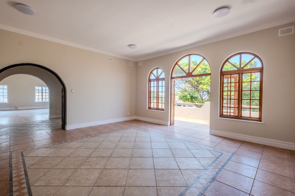 Spacious, light-filled living area featuring tiled floors, elegant arched timber windows, and direct access to an outdoor balcony through classic french doors.