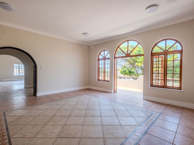 Spacious, light-filled living area featuring tiled floors, elegant arched timber windows, and direct access to an outdoor balcony through classic french doors.
