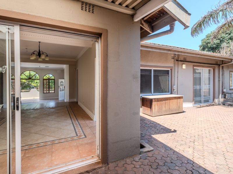 A paved outdoor patio area featuring sliding glass doors that open into a spacious, tiled interior living space with arched windows.