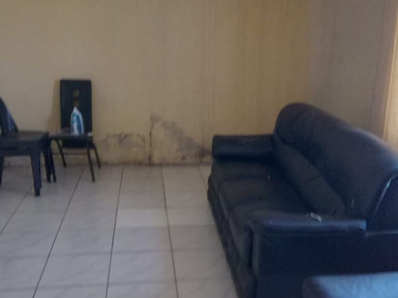 A living room area featuring tiled flooring and visible wall damage requiring maintenance and cosmetic repair.