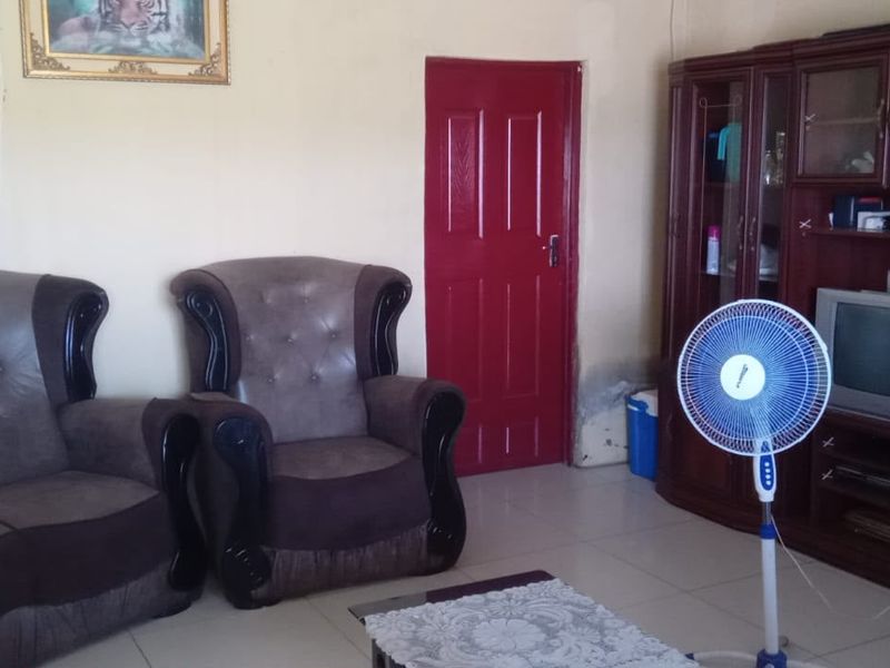 A living room featuring tiled flooring and a painted internal door, showing signs of wear on the lower wall surfaces.