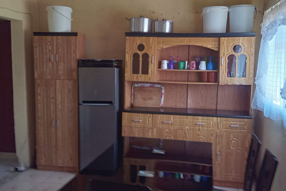 A kitchen area featuring built-in wooden cabinetry and basic finishes, currently showing signs of wear and requiring cosmetic updates.