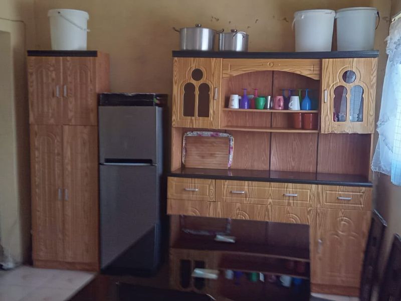 A kitchen area featuring built-in wooden cabinetry and basic finishes, currently showing signs of wear and requiring cosmetic updates.