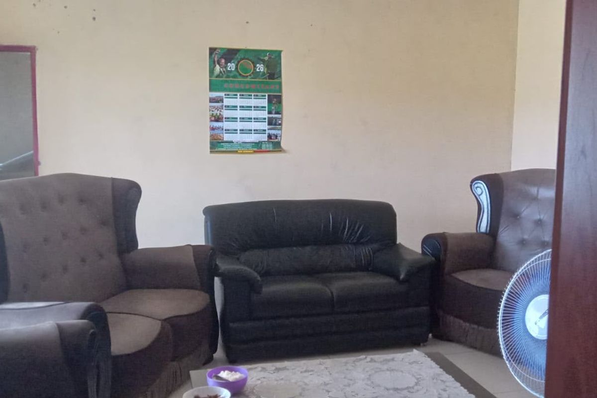 A living room area featuring plain walls and tiled flooring, currently furnished with a seating arrangement.