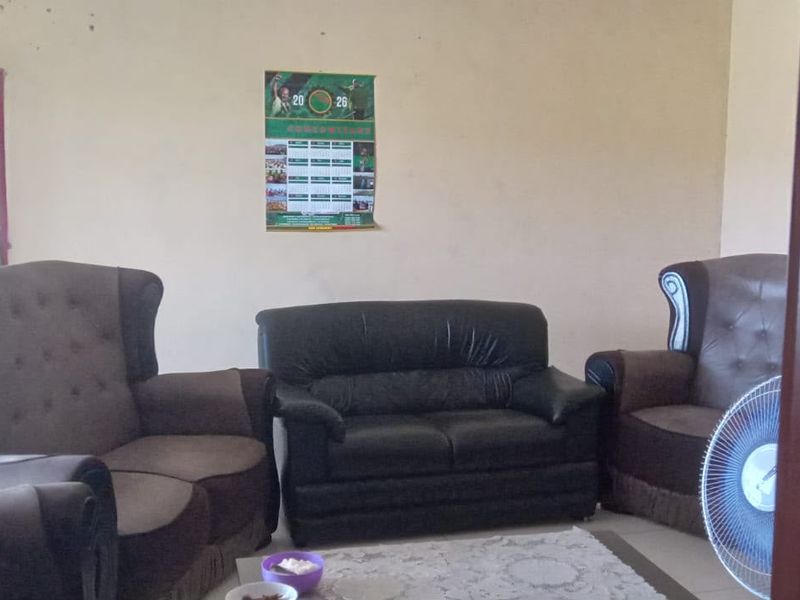 A living room area featuring plain walls and tiled flooring, currently furnished with a seating arrangement.