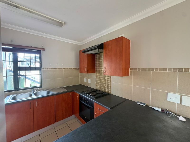 A functional kitchen featuring laminate cabinetry, dark countertops, built-in oven and hob, tiled backsplash, and a double sink with security bars on the window.