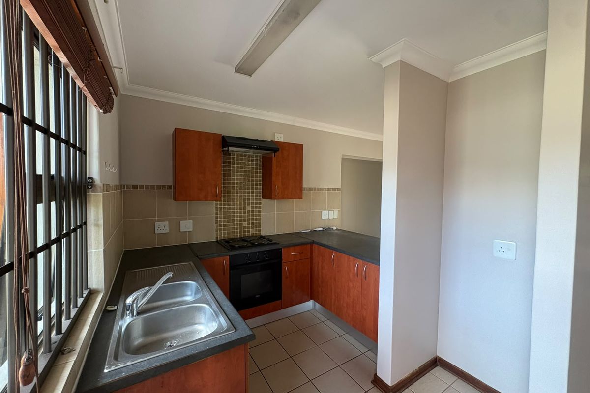 A functional kitchen featuring built-in wooden cabinetry, a double sink, gas hob, and oven, finished with tiled splashbacks and flooring.
