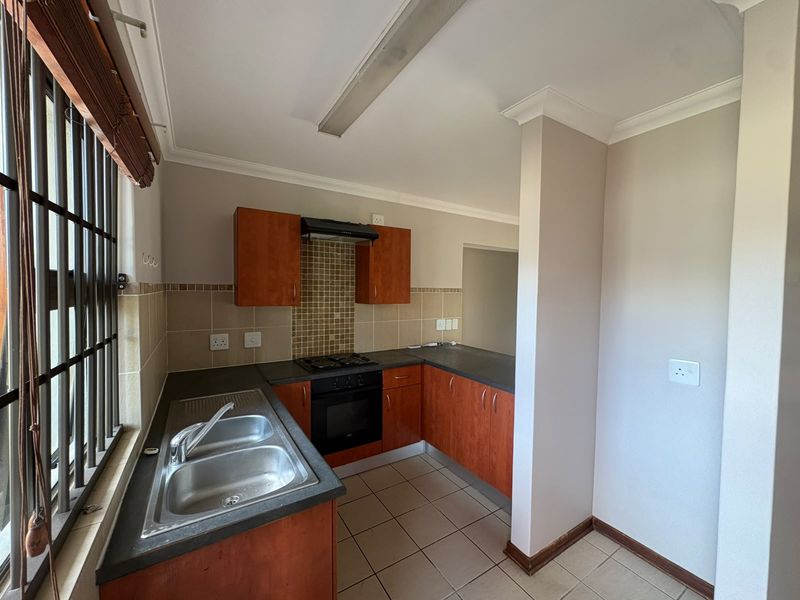 A functional kitchen featuring built-in wooden cabinetry, a double sink, gas hob, and oven, finished with tiled splashbacks and flooring.