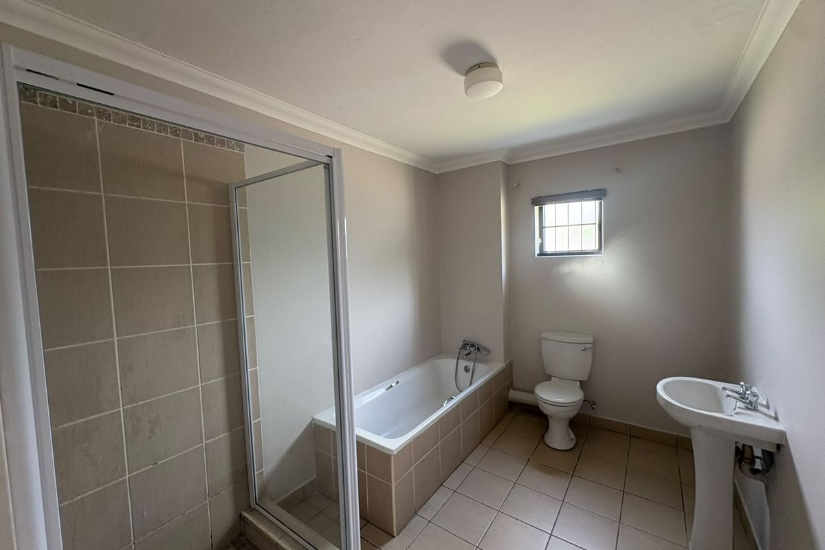 A functional bathroom featuring a built-in bathtub, separate shower enclosure, pedestal basin, and toilet with neutral tiled finishes.