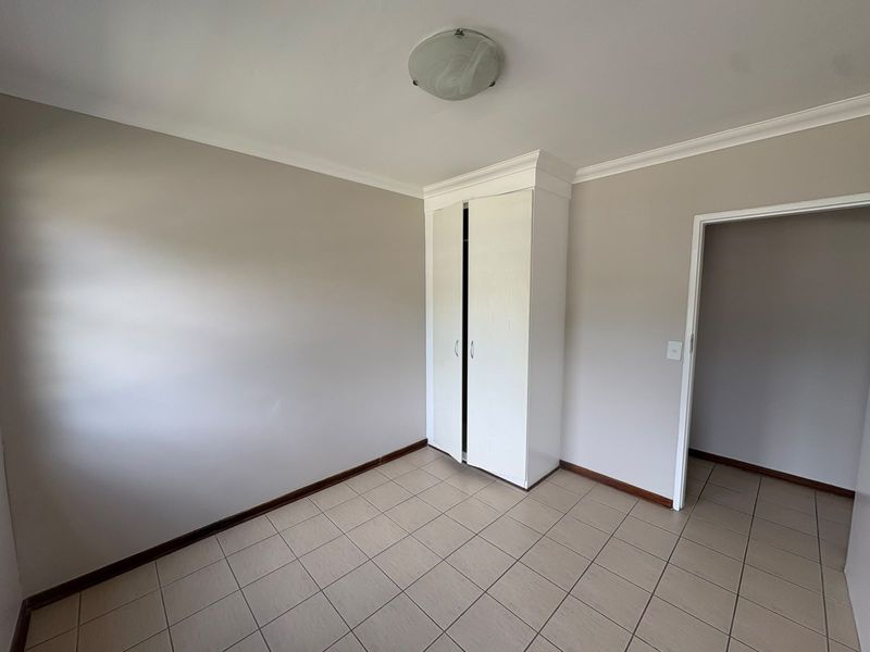 An empty bedroom featuring neutral wall paint, tiled flooring, and a built-in wardrobe with white cabinetry.