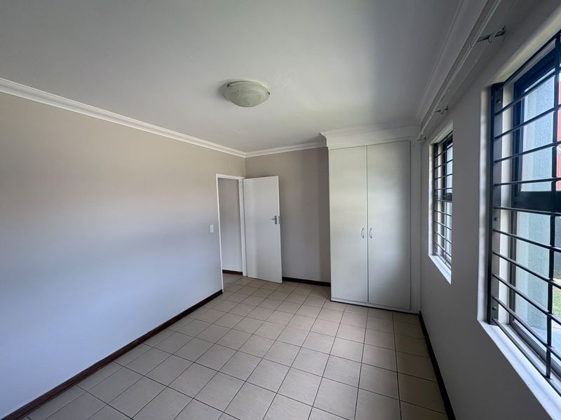 A clean, empty bedroom featuring neutral tiled flooring, built-in cupboards, and security bars on the windows, offering a blank canvas for personalization.