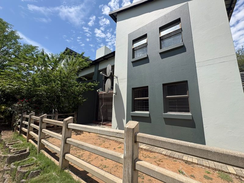 Rear exterior view of the townhouse featuring a two-tone painted facade, security bars on windows, and a concrete perimeter fence.