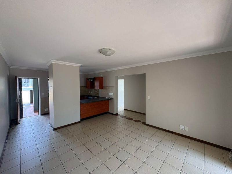 An open-plan living and kitchen area featuring neutral wall tones, tiled flooring, and built-in wooden cabinetry, offering a functional and versatile living space.