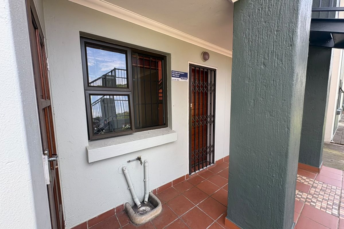 Covered patio area featuring tiled flooring, a security gate, and an external water tap with a drainage basin.