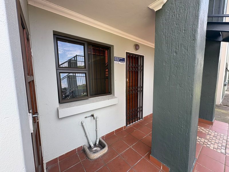 Covered patio area featuring tiled flooring, a security gate, and an external water tap with a drainage basin.