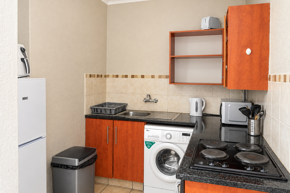 Compact kitchen featuring wooden cabinetry, dark laminate countertops, tiled backsplash, and integrated laundry plumbing, providing a functional and efficient workspace.