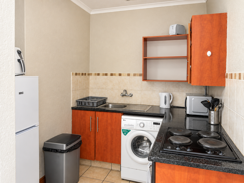 Compact kitchen featuring wooden cabinetry, dark laminate countertops, tiled backsplash, and integrated laundry plumbing, providing a functional and efficient workspace.