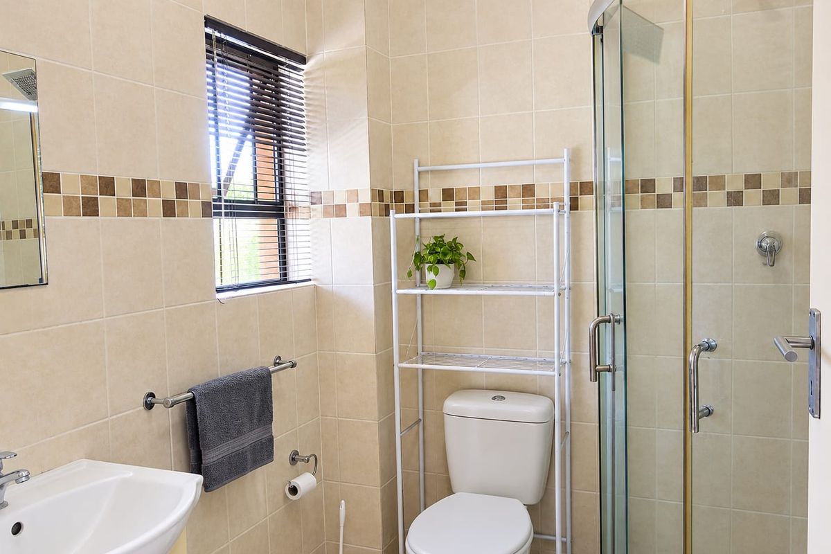 A functional bathroom featuring a glass shower enclosure, pedestal basin, and neutral ceramic wall tiling with a decorative mosaic border.
