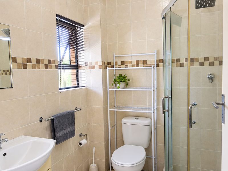 A functional bathroom featuring a glass shower enclosure, pedestal basin, and neutral ceramic wall tiling with a decorative mosaic border.