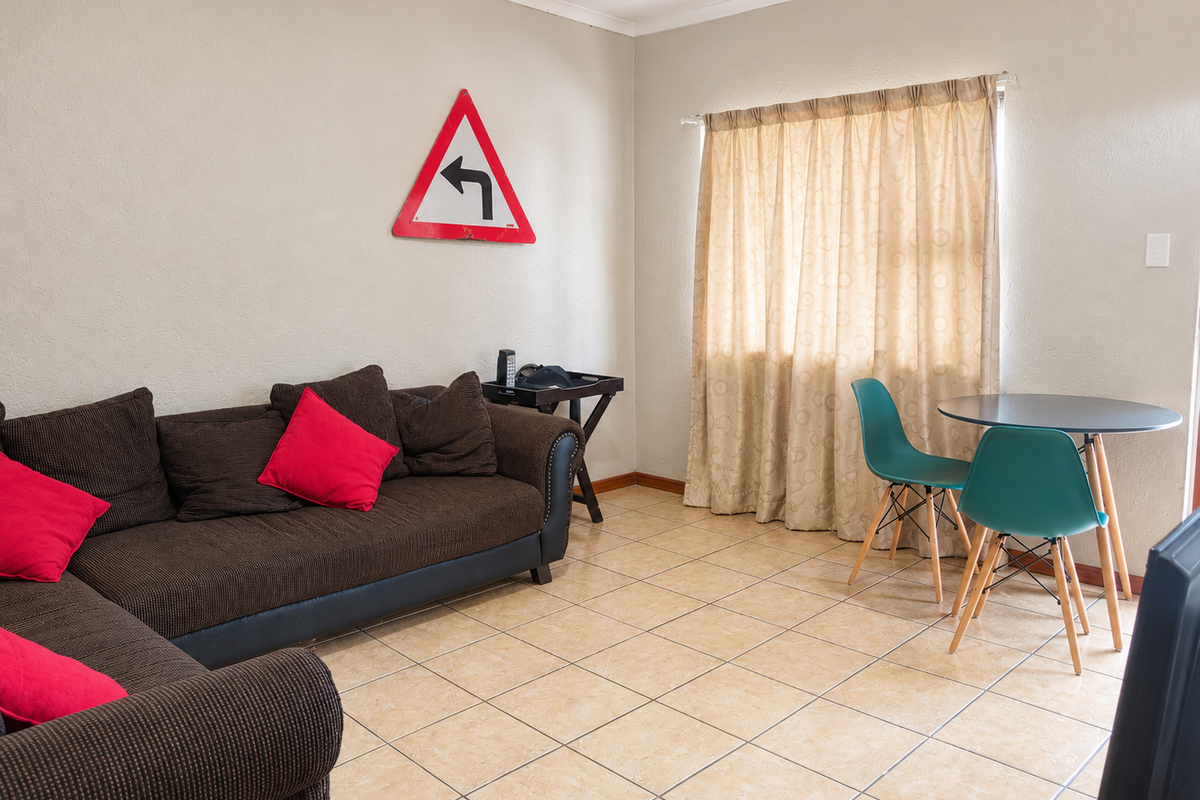 A living room area featuring neutral wall tones and tiled flooring, with a window dressed in curtains.