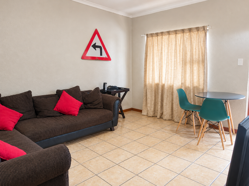A living room area featuring neutral wall tones and tiled flooring, with a window dressed in curtains.