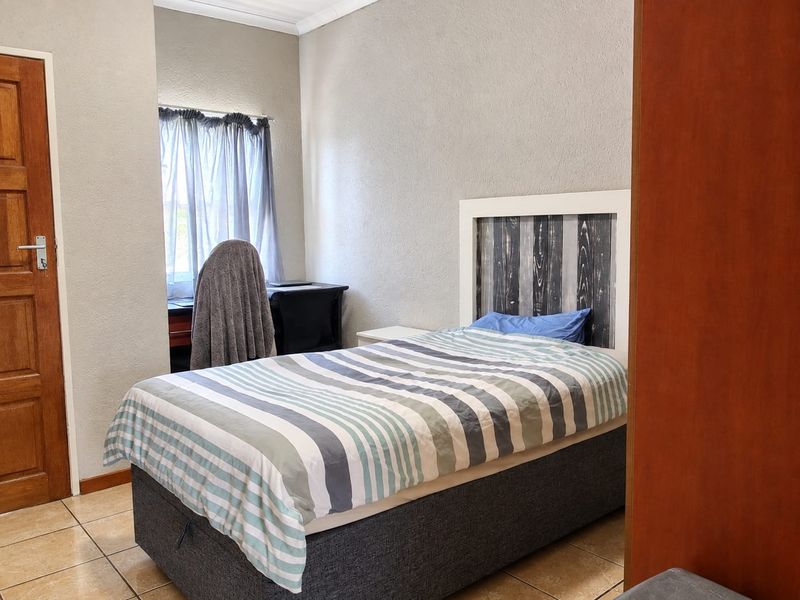 A functional bedroom featuring tiled flooring, a window, and a standard door, providing a comfortable and practical living space.