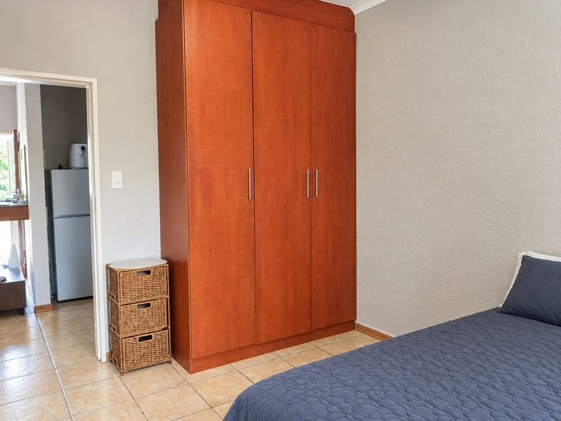 A bedroom featuring a large built-in wooden wardrobe and tiled flooring, with a doorway leading to an adjacent kitchen area.