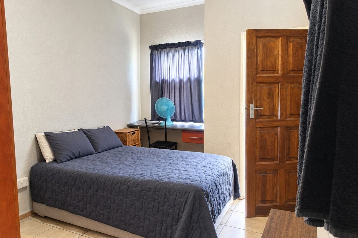 A functional bedroom featuring tiled flooring, a built-in desk area, and a solid timber door.