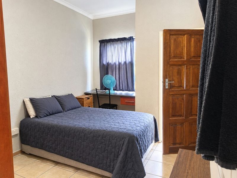 A functional bedroom featuring tiled flooring, a built-in desk area, and a solid timber door.