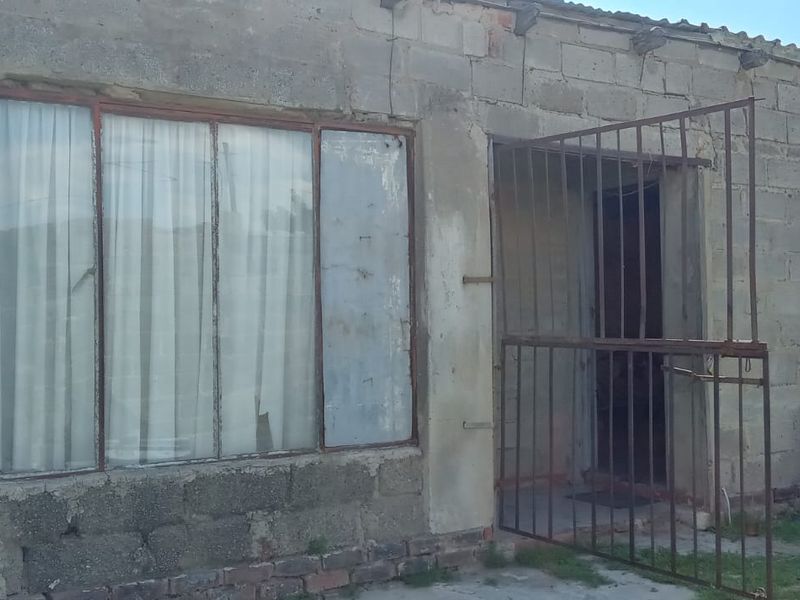 Front elevation of a single-story house featuring exposed concrete block construction, metal window frames, and a security gate entrance.