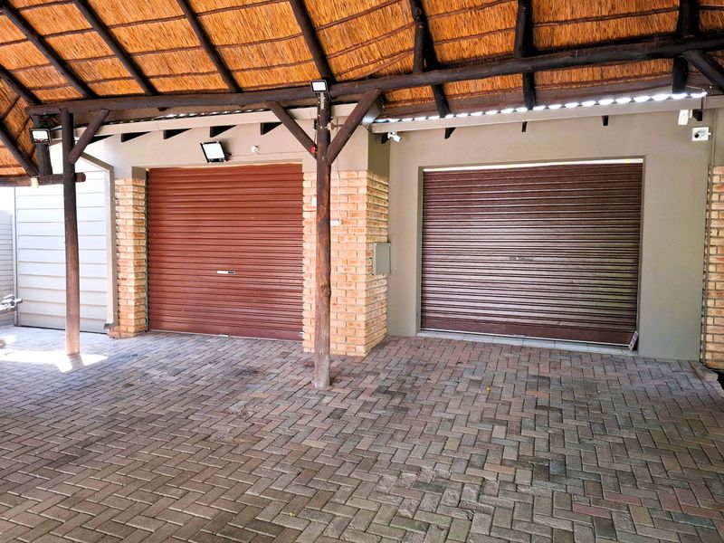 A well-maintained double garage featuring secure roller doors, a traditional thatched roof structure, and durable paved flooring.