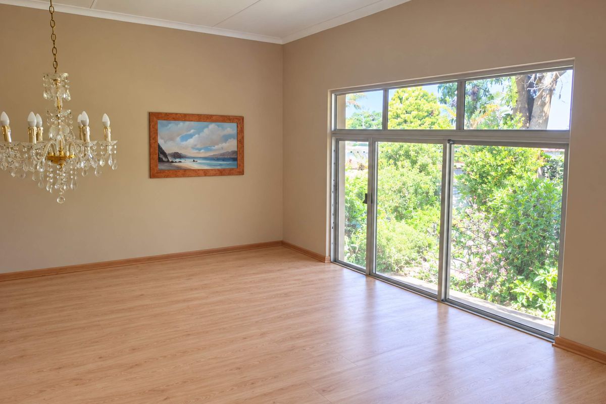 Spacious living area featuring light wood-look laminate flooring, a classic crystal chandelier, and large sliding glass doors providing ample natural light and garden views.